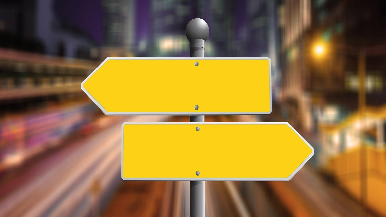 Two yellow road signs on a sign post. The top sign points to the left and the bottom sign points to the right.